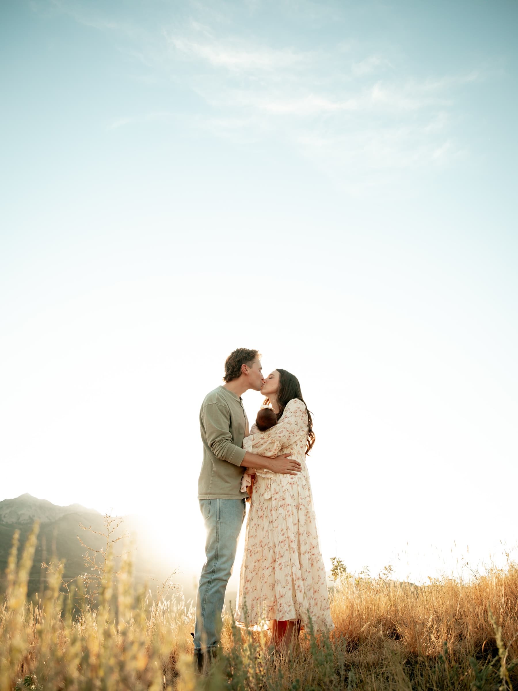 A couple holds one another in a sunlit field.