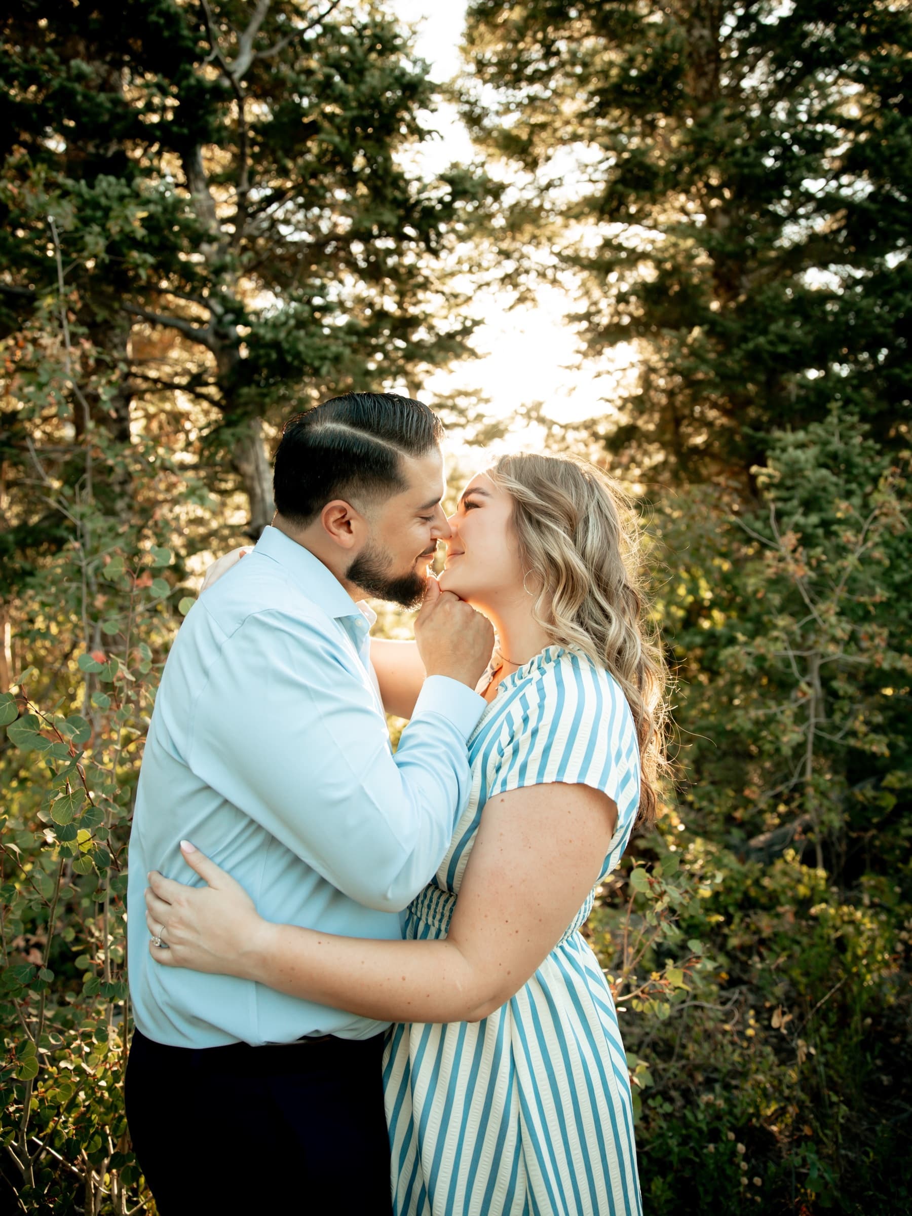 A couple shares a quiet kiss among evergreen trees.