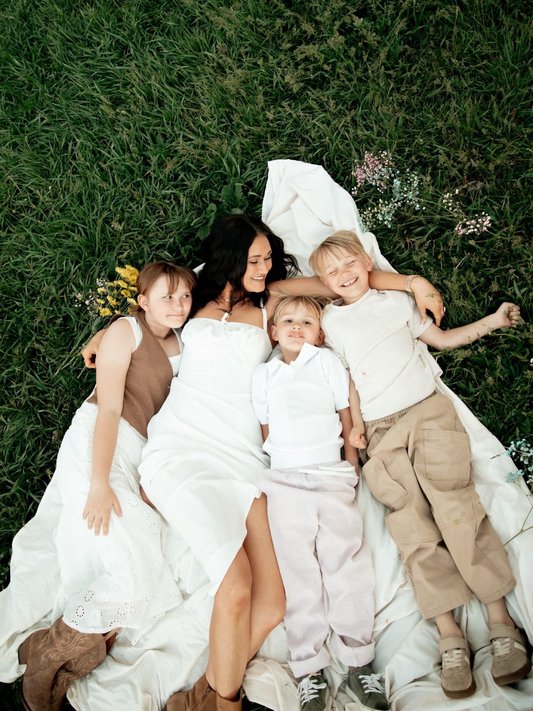 A family lies together on a blanket in green grass.