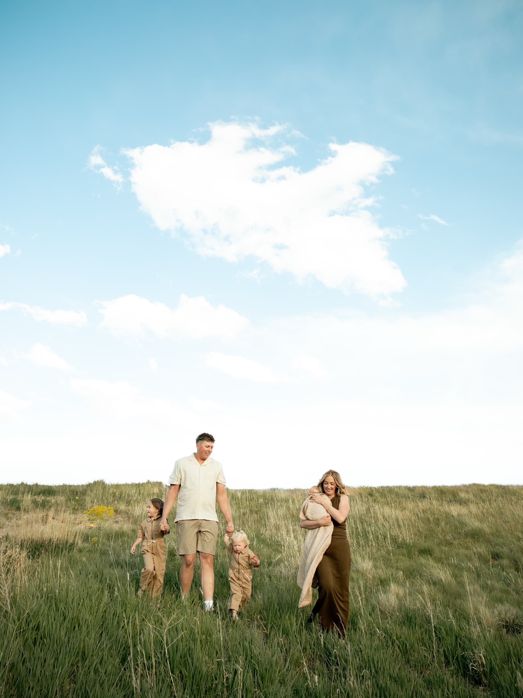 A family walks together through a wide green field beneath an open sky.