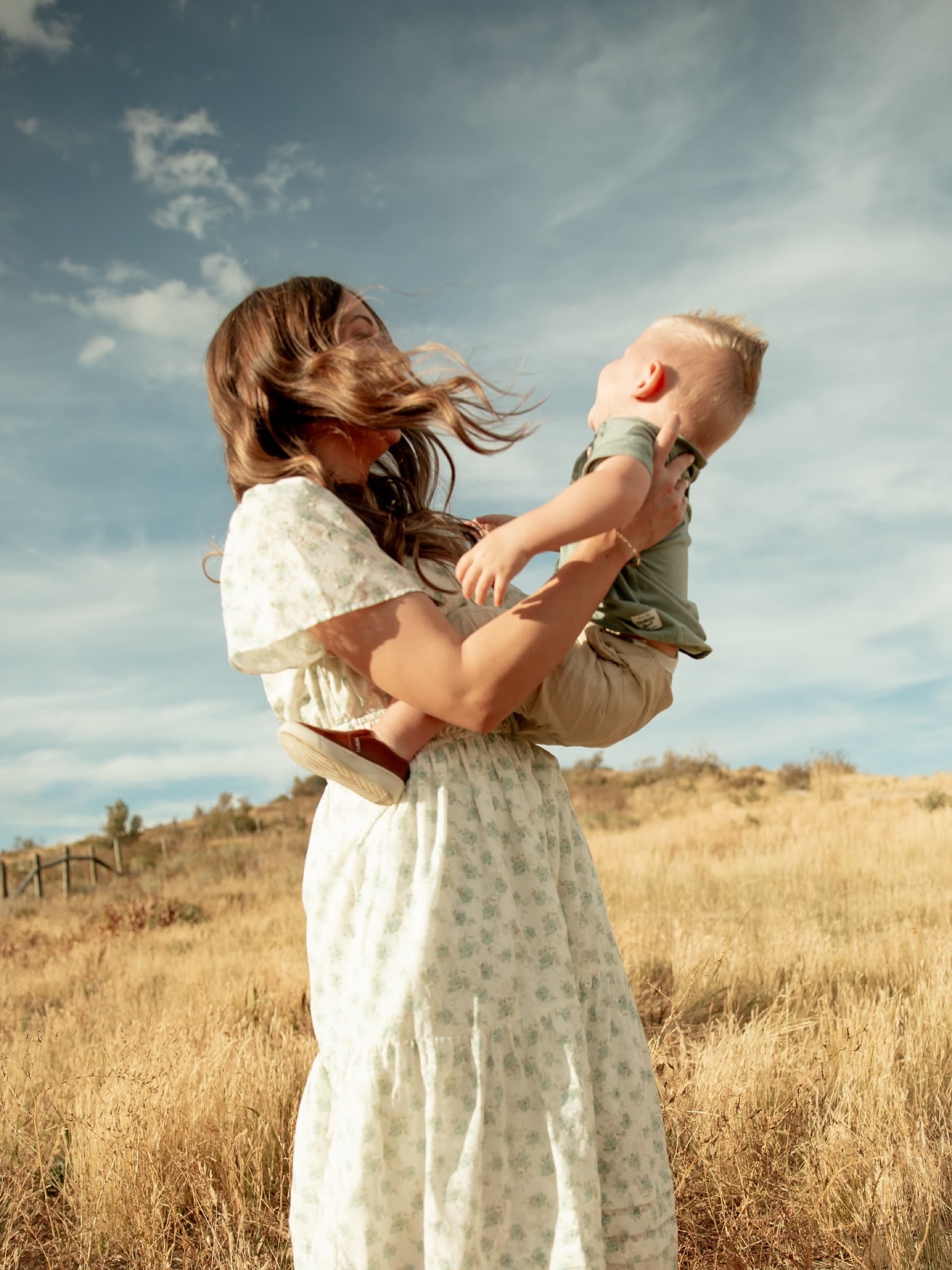 A mother lifts her laughing toddler into a bright blue sky.