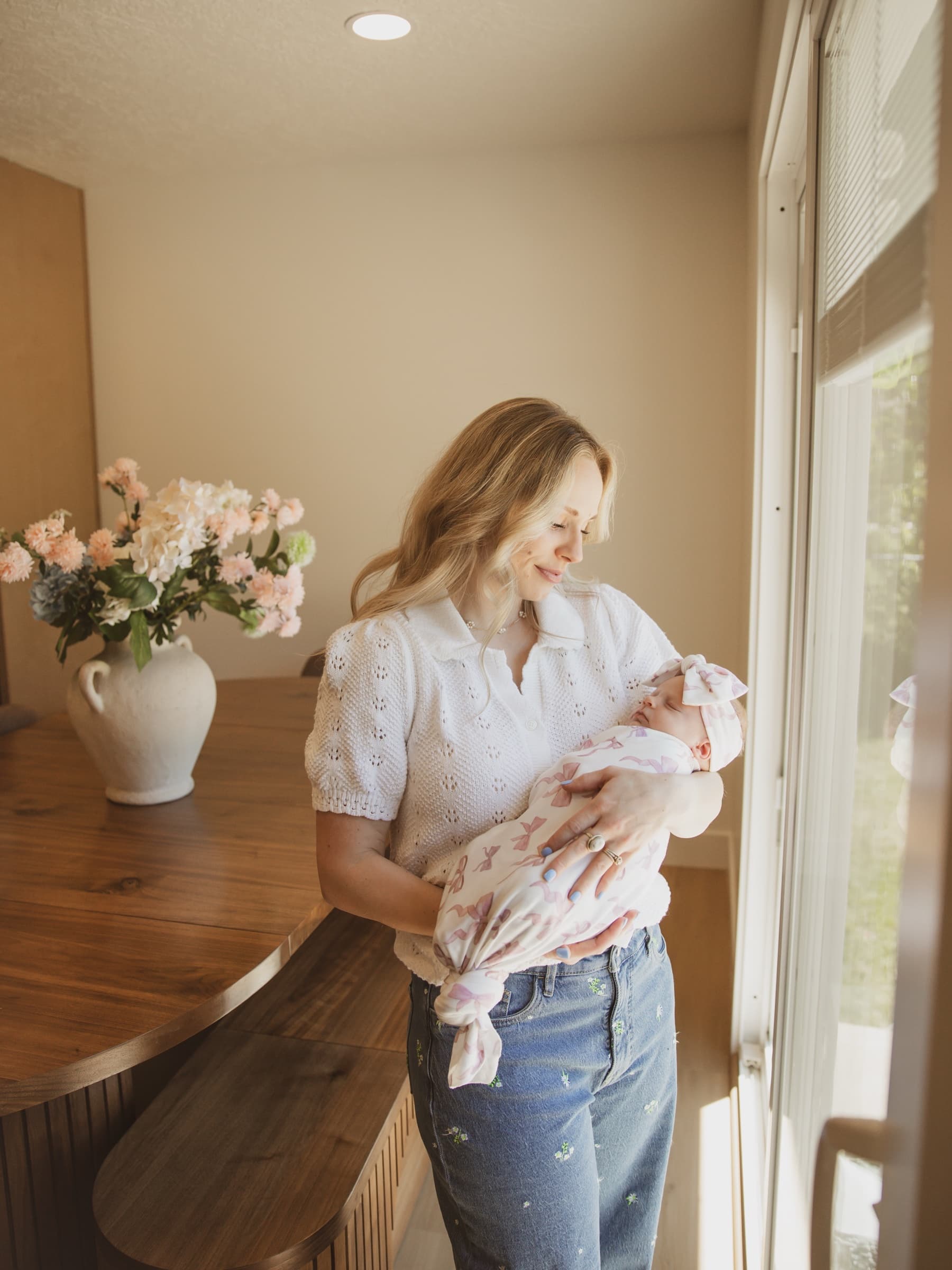 A mother cradles her newborn beside a softly lit window.