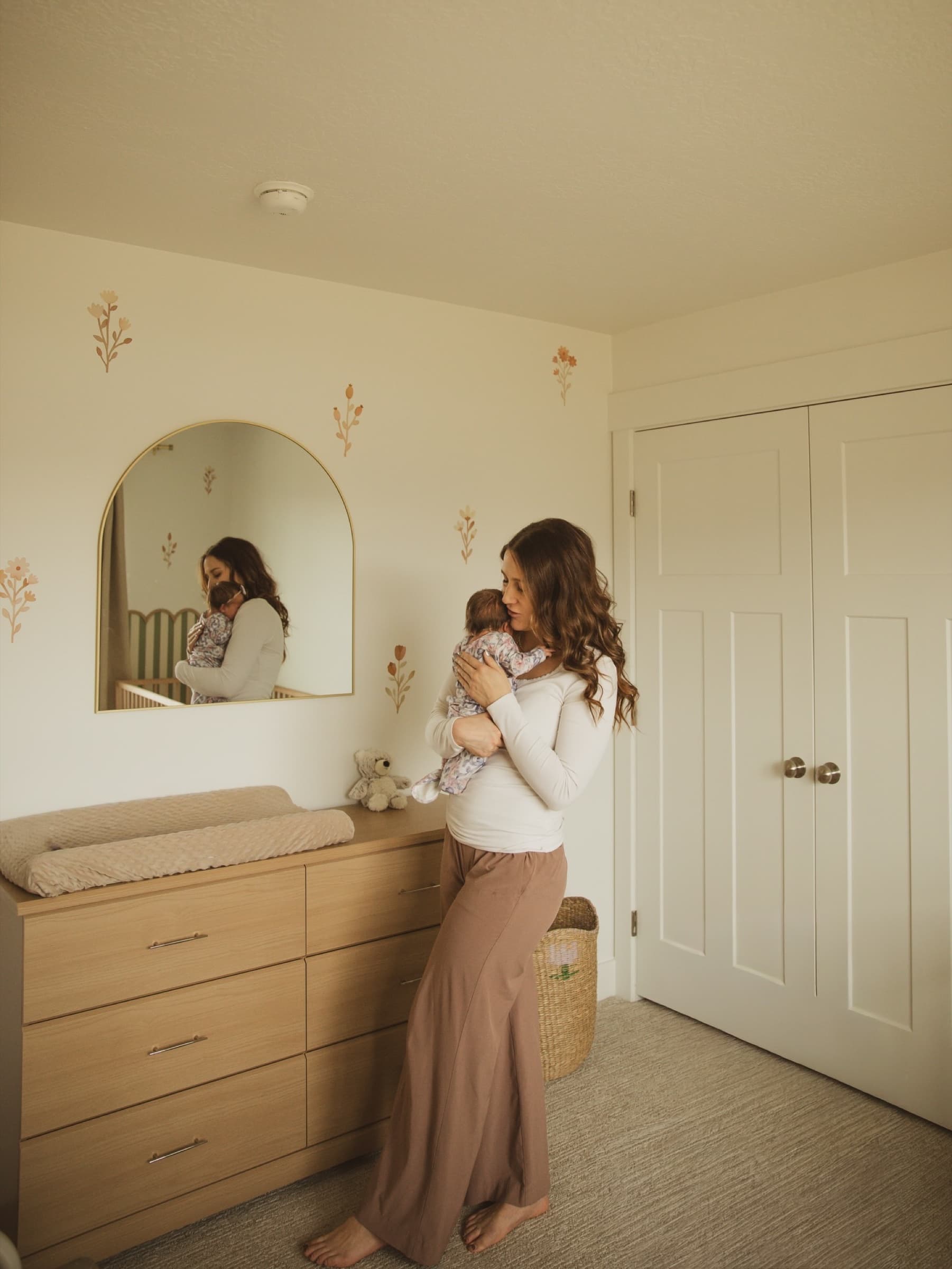 A mother holds her baby in a softly lit nursery.