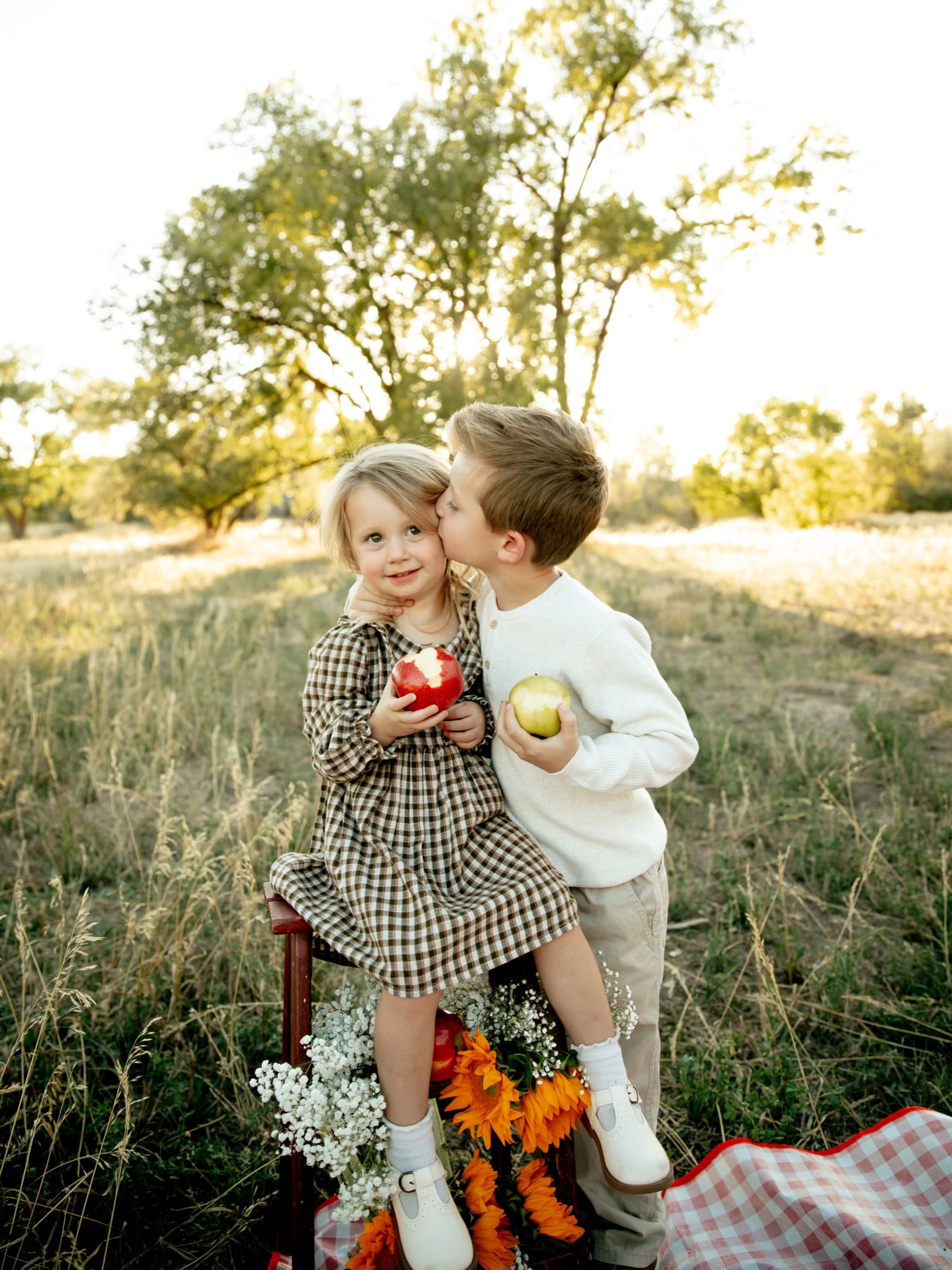 Two young siblings sit together on a picnic blanket.