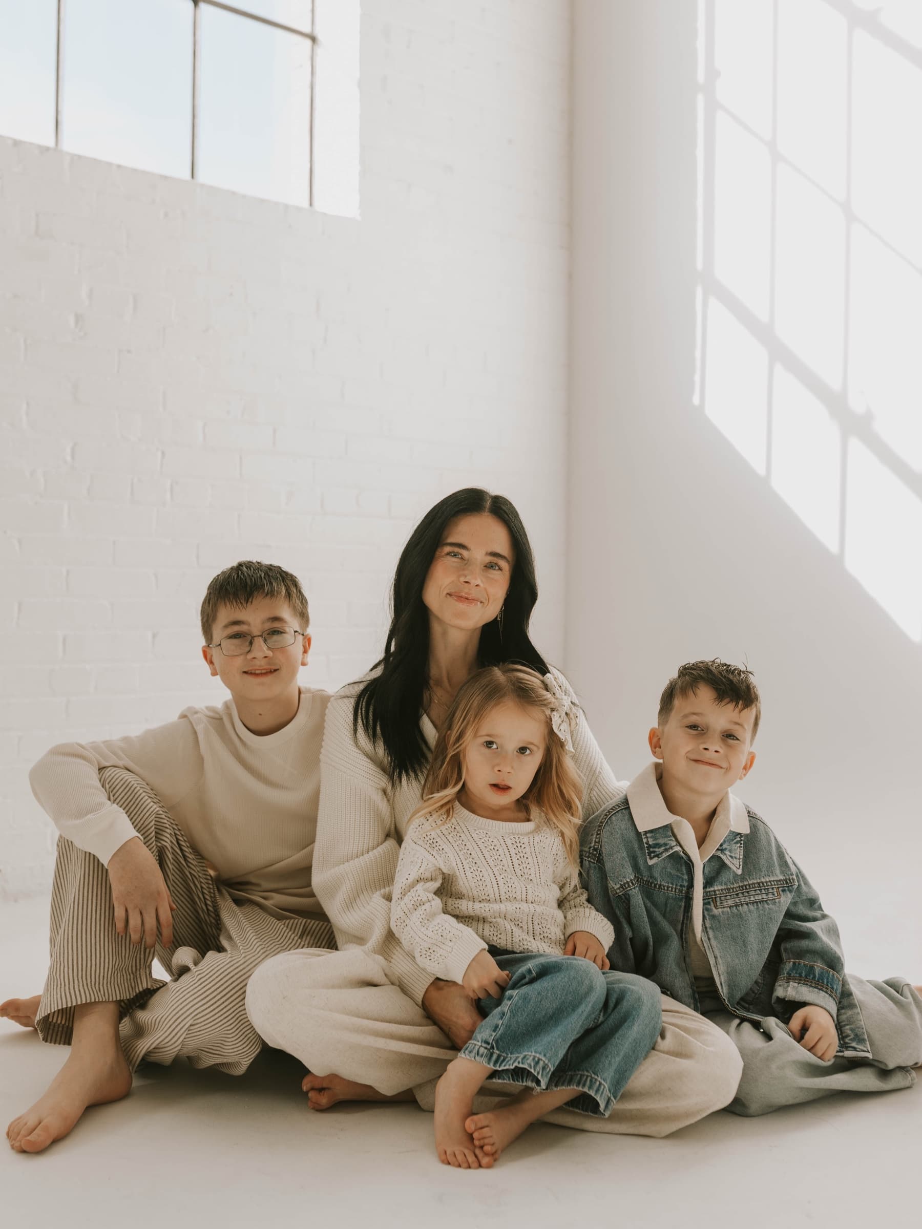 Children sit closely with their mother in a bright studio window.